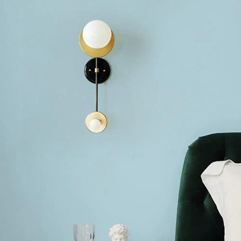 Modern black and gold wall light fixture with opal glass globe and metal accents for bedroom use