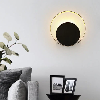 Modern black and gold metallic orbit sconce light with sleek center and warm rim emitting soft ambient light