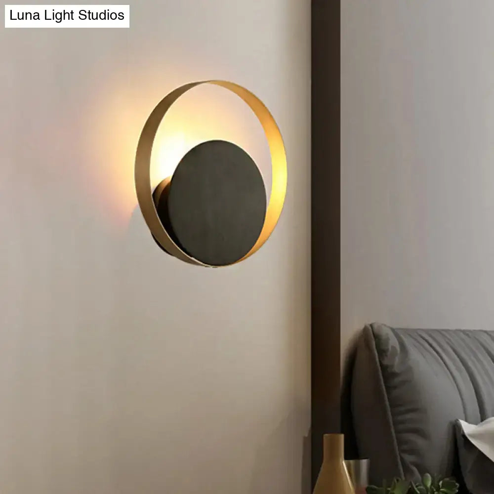 Modern black and gold metallic orbit sconce light with a gold-toned circular frame and matte black central disc for ambient living room lighting