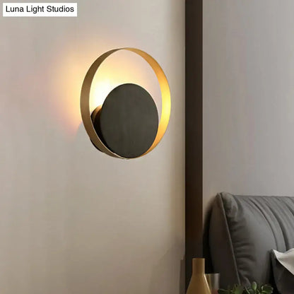 Modern black and gold metallic orbit sconce light with a gold-toned circular frame and matte black central disc for ambient living room lighting