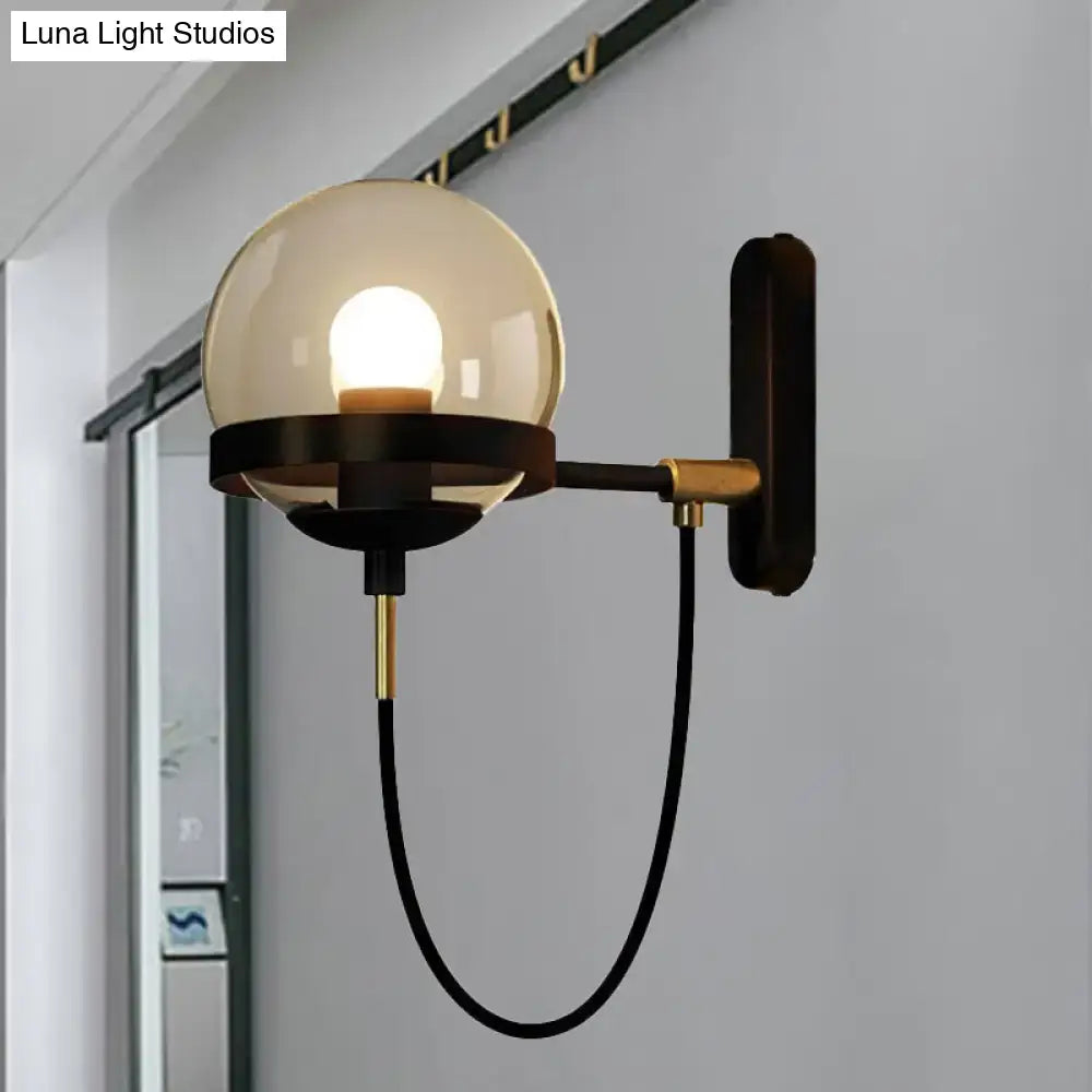 A modern black gold wall lamp with a smoke glass amber globe and metal arm for living room sconce lighting
