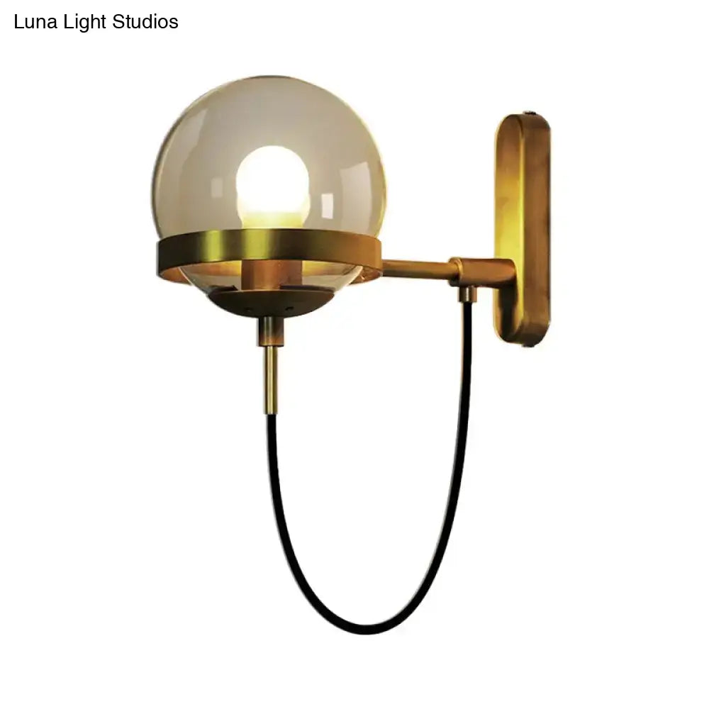 A warm-toned black gold wall lamp with smoke glass spherical globe and black cord for modern living room sconce
