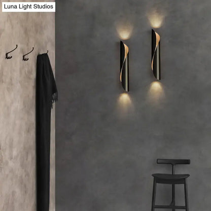 Two sleek black and gold modern twisted wall sconce lights emit warm light on gray textured corridor walls
