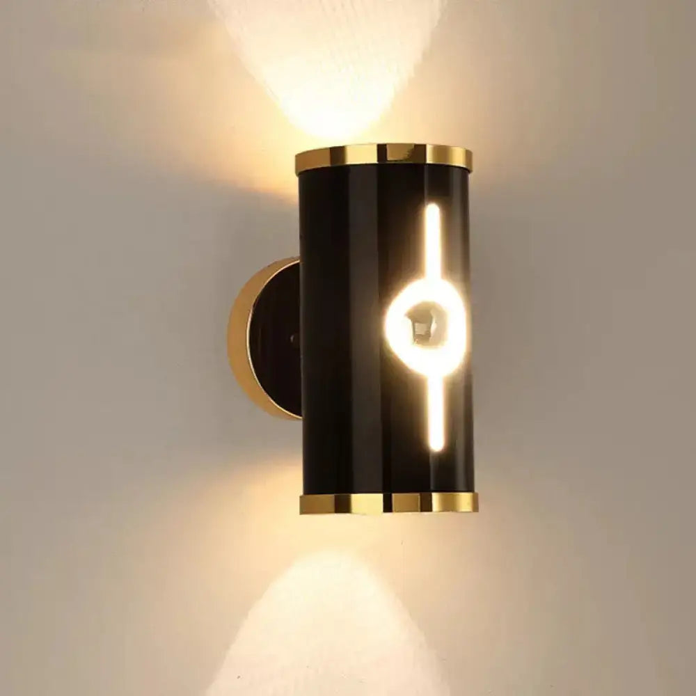 Modern black and gold wall lamp with black finish, cylindrical design, gold-toned accents, and vertical light strip for bedroom