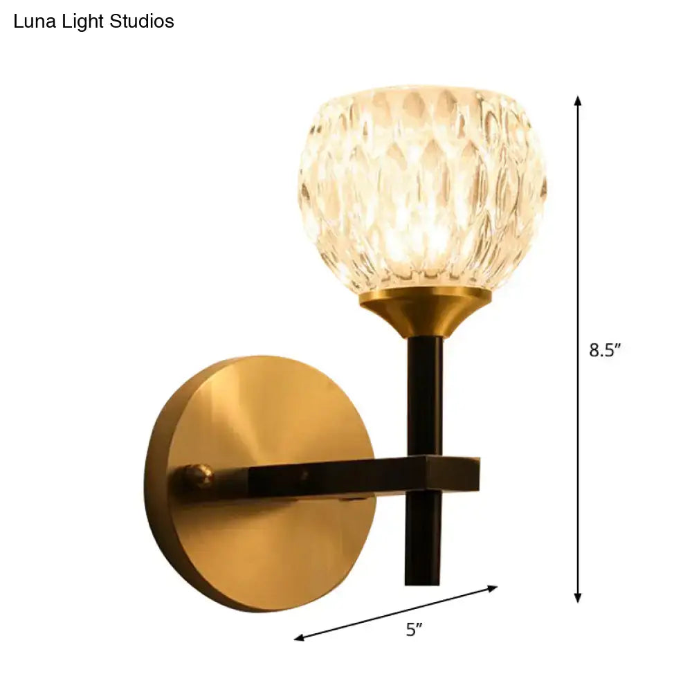 Gold-toned wall light with faceted dimpled glass shade and black metal arm for living room illumination