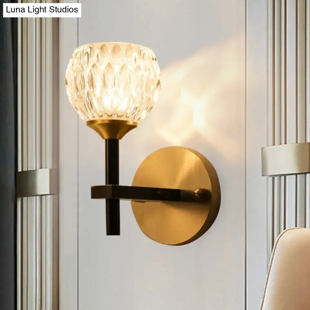 A modern black and gold wall light with dimpled crystal glass shade and brass base for living room use