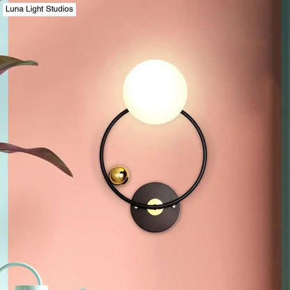 Modern black and gold wall sconce light featuring an opal glass shade with a glowing white spherical bulb and gold accents