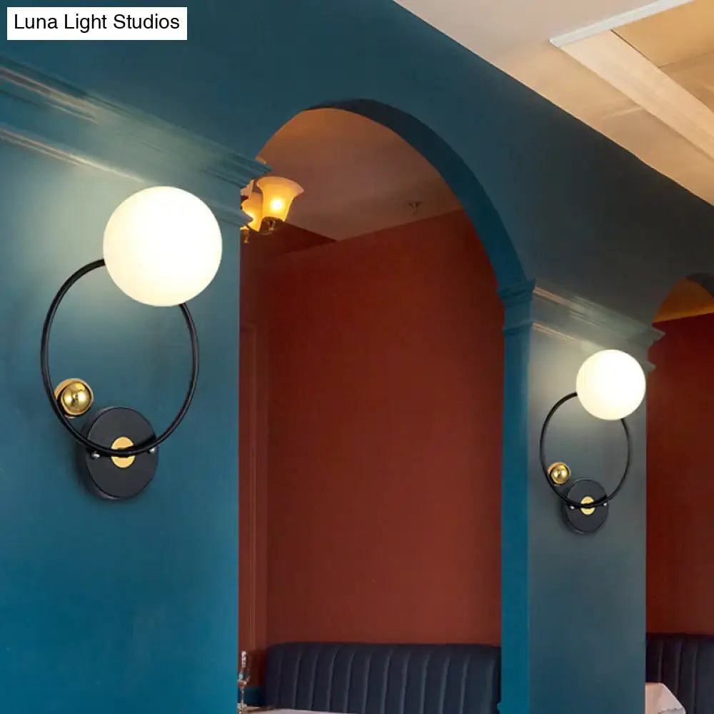 Modern black and gold wall sconce light with opal glass shade featuring a frosted white spherical glass globe for bedroom use