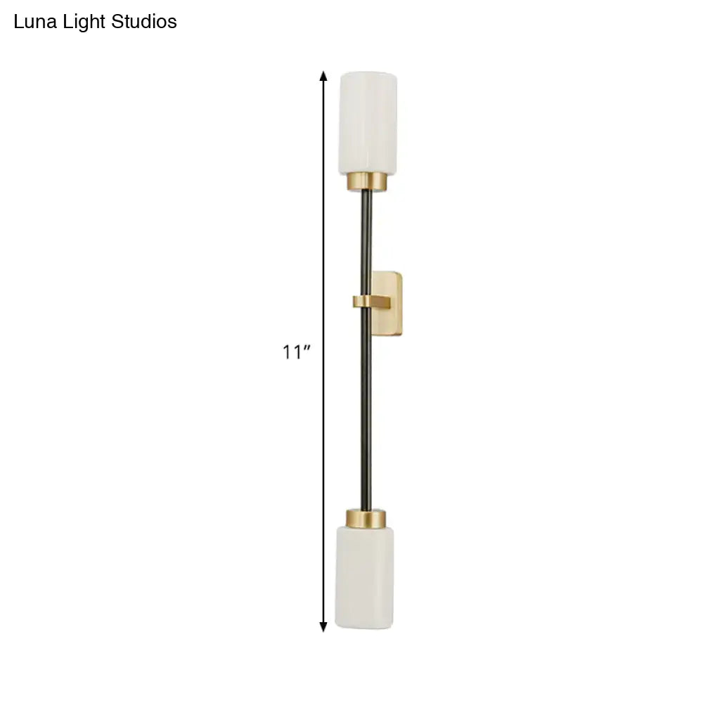 A modern black and gold wall sconce with white glass shade and cylindrical off-white glass for living room decor