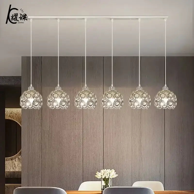 Five elegant crystal dining pendant lamps with intricate patterns hang from a modern black iron cage ceiling bar