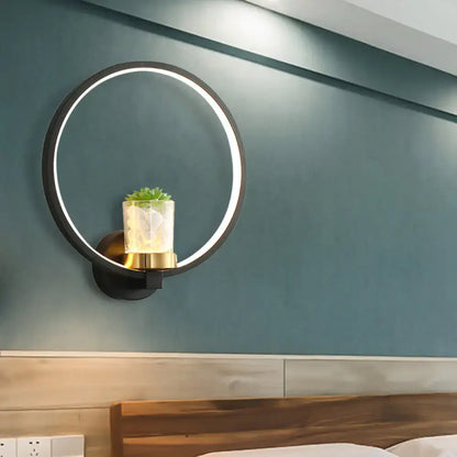 Modern black led light circular wall sconce with gold base holding a clear glass vase with greenery for bedroom use