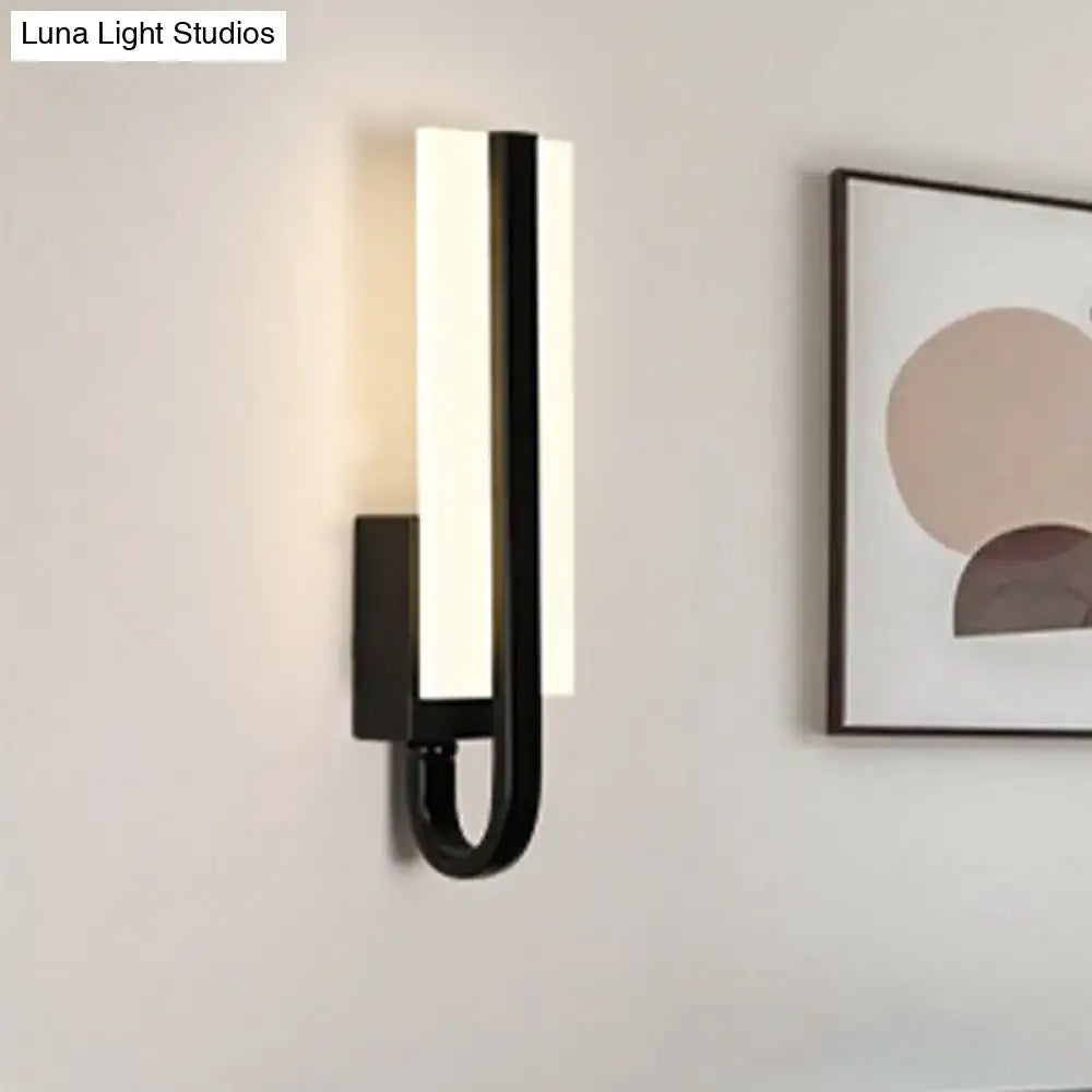 Modern black metal sconce light fixture with sleek curved design and glowing white warm light panel for living room