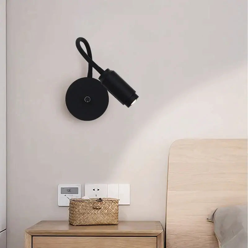 Black wall lamp with sleek curved arm and adjustable focus led spotlight for modern bedroom lighting