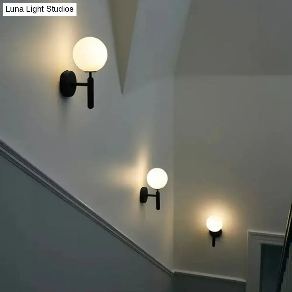 Modern black matte wall sconce with frosted glass globe and black gold accents for stairs lighting