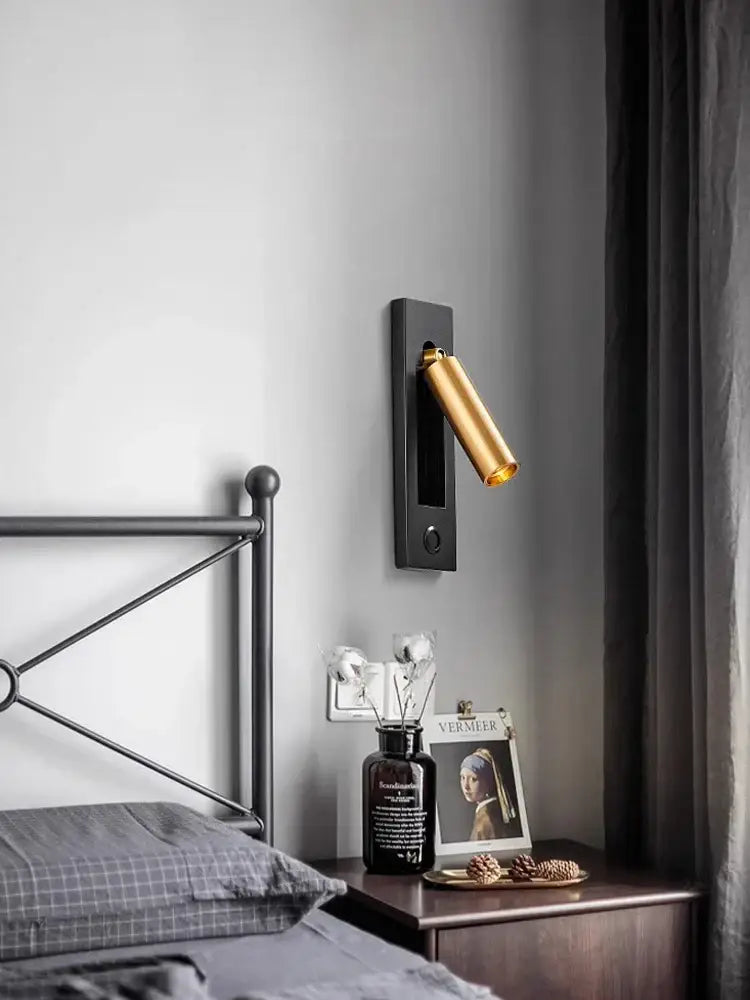 A sleek black metal led wall lamp with a gold cylindrical head and usb port for bedroom reading light