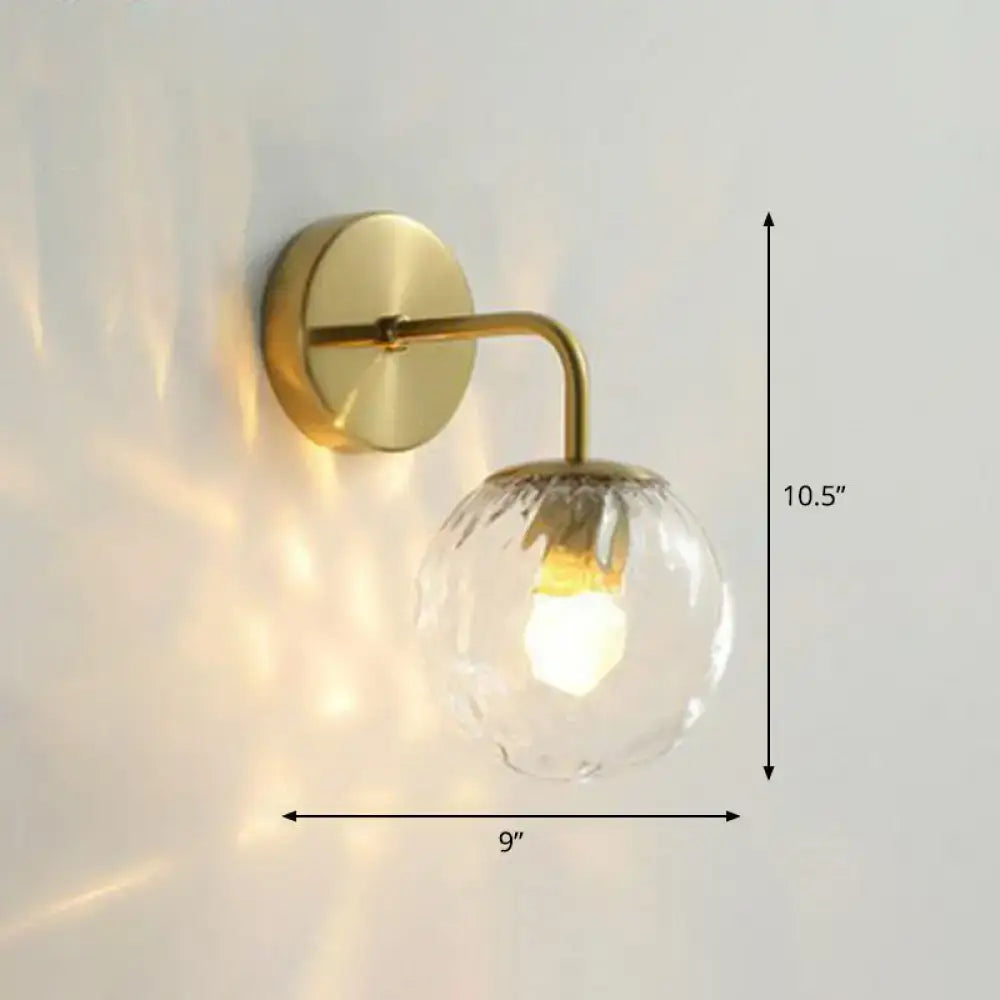 A sleek brass wall mount light with a clear faceted glass globe and illuminated bulb for modern bedroom use