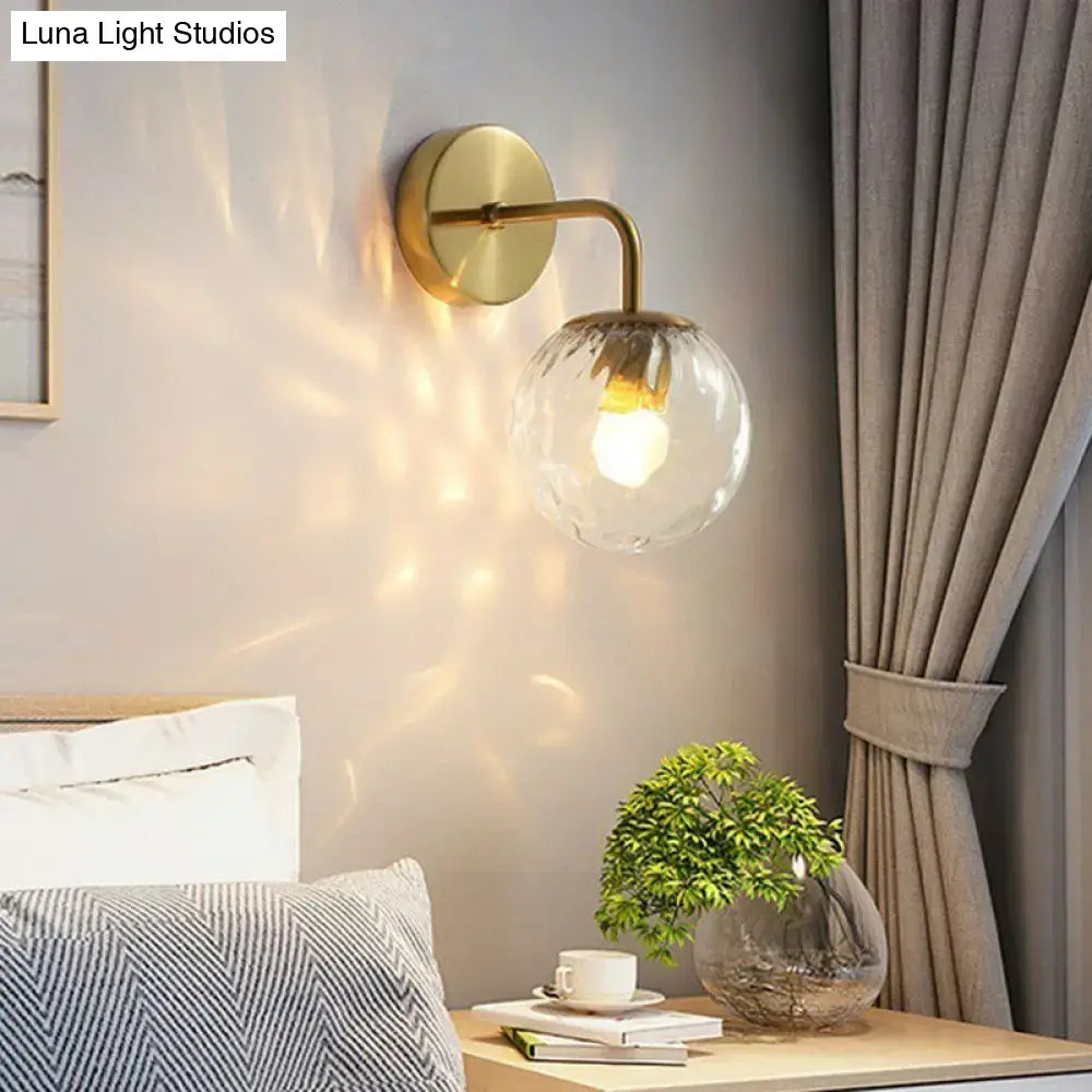 Modern black metal wall mount light with brass finish and textured glass globe shade for bedroom sconce lighting