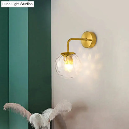Gold-toned wall mount light with clear faceted glass globe and modern black metal rippled glass design for bedroom use