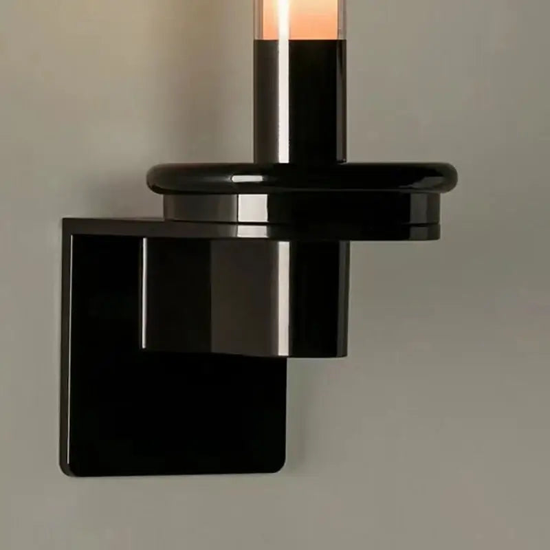 Modern black metal wall light with clear glass shade and sleek geometric design featuring a central illuminated cylinder