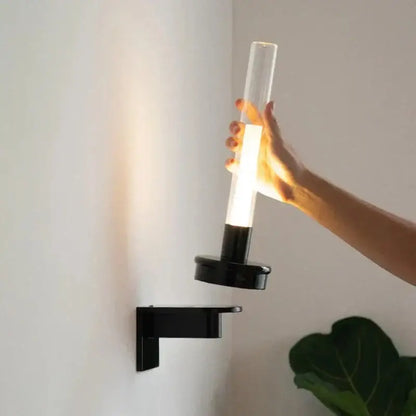 Modern black metal wall light with clear glass shade and cylindrical tube designed for bedroom lighting