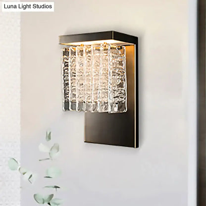 Modern black metal wall sconce with vertical crystal prism rods catching light in a living room 12 inch fixture