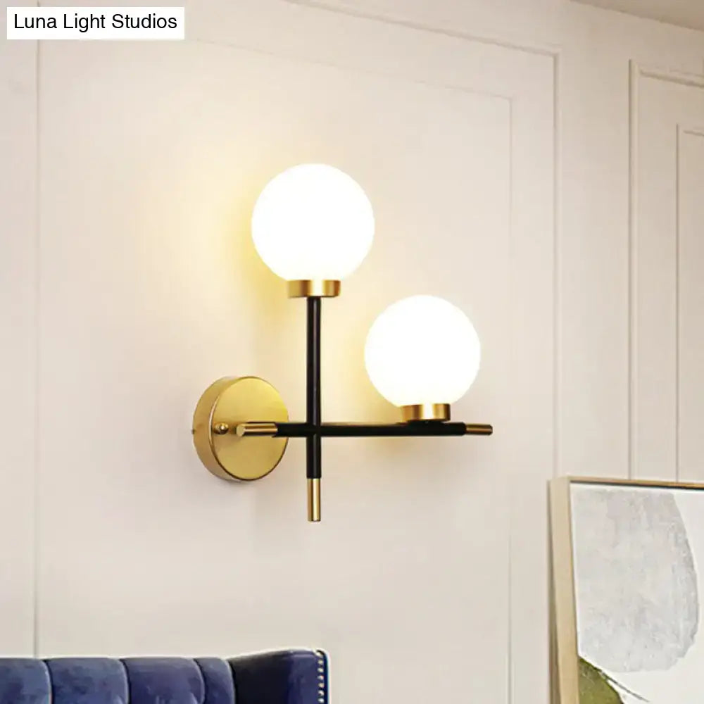Modern black wall mount light fixture with milk glass frosted globe shades and gold accented two-light sconce design