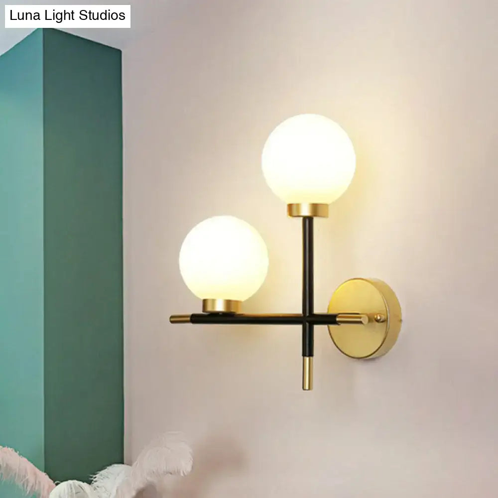 Modern black two-light wall mount sconce with frosted milk glass globes and gold metal frame for foyer lighting fixture