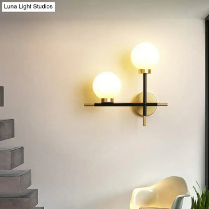 Modern black wall mount light fixture with two milk glass frosted globes and gold toned hardware for foyer use