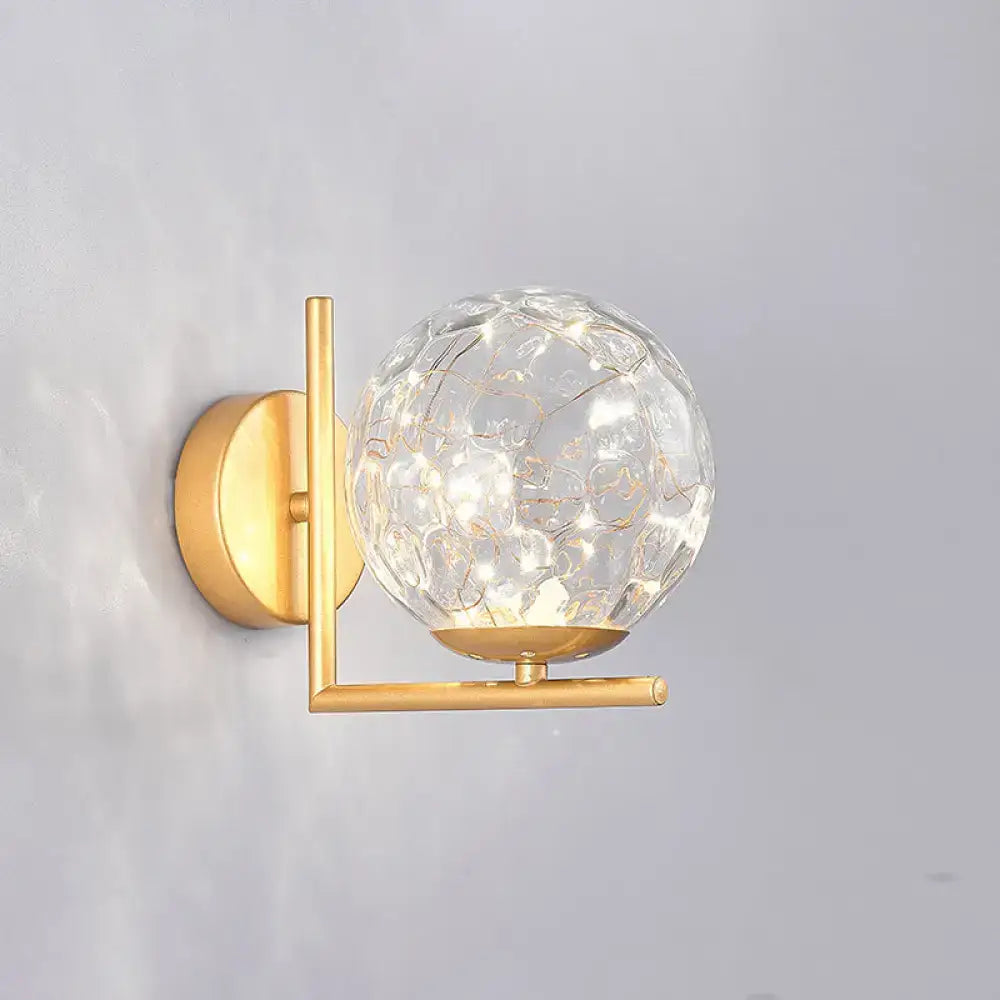 Gold-toned mini globe wall sconce with textured crackled glass globe and modern fixture height for bedroom lighting