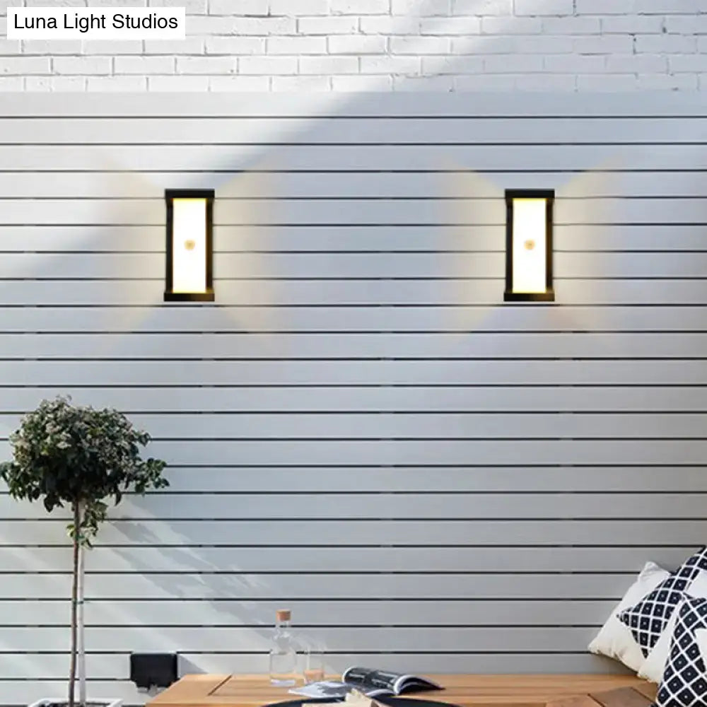 Two sleek modern black outdoor LED wall lamps with rectangular frosted light emit warm white glow on horizontal siding
