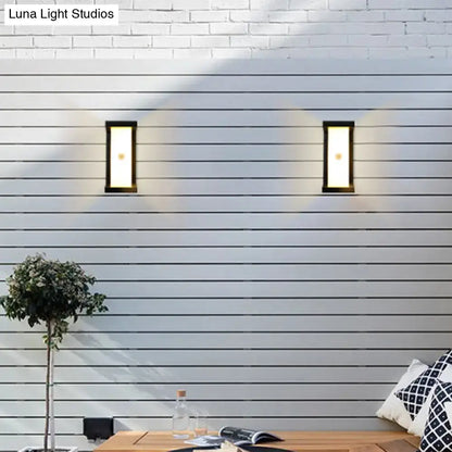 Two sleek modern black outdoor LED wall lamps with rectangular frosted light emit warm white glow on horizontal siding