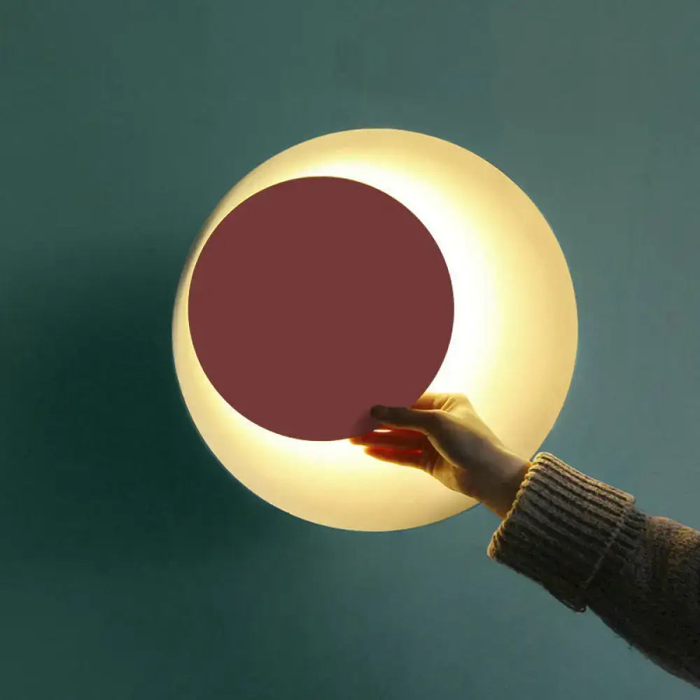 Modern black and pink circle sconce light fixture with a matte white shell and warm glowing maroon inner circle for bedroom use