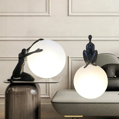 Two matte black minimalist table lamps with sculptural figures atop glowing white glass ball holders for decorbites abstract humanoid decor