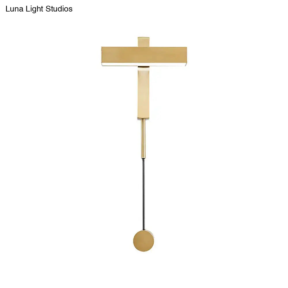 Gold-toned modern wall lamp with minimalist t-shaped bulb base and adjustable arm mounted on a circular base for bedroom use