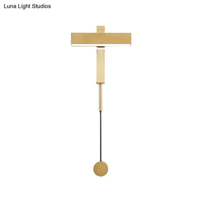 Gold-toned modern wall lamp with minimalist t-shaped bulb base and adjustable arm mounted on a circular base for bedroom use