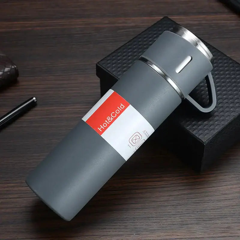 Gray insulated travel mug with stainless steel lid and handle featuring red and white hot and cold label vacuum insulated water bottle