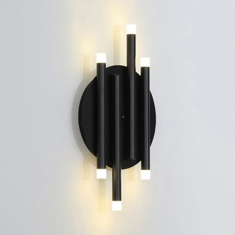 Modern black wall light with round backplate featuring four vertical cylindrical bulb bases emitting warm light