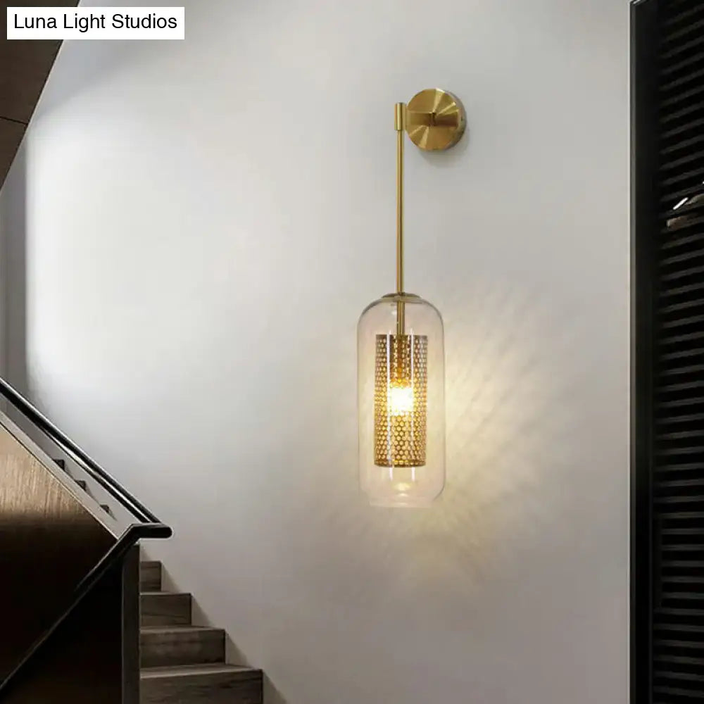Modern black wall sconce with clear glass cylindrical shade and intricate gold-toned perforated wire mesh interior
