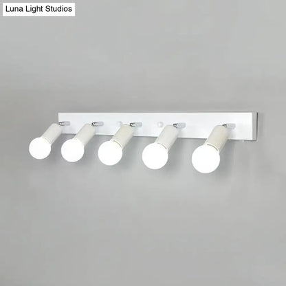 Modern black and white bedroom vanity light fixture with five exposed frosted glass cylindrical bulbs mounted on white wall