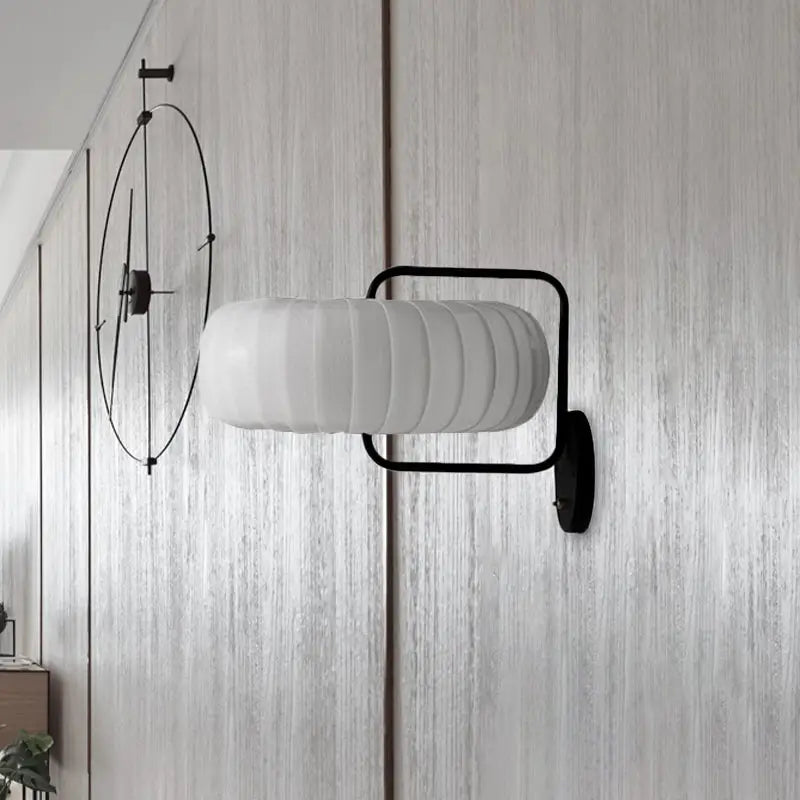 Modern black metal wall sconce with frosted white ribbed glass shade and gathered fabric pumpkin design for bedroom light