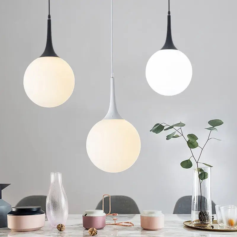 Three modern black and white decorbites glass ball pendant lamps with frosted glass shades hang above a dining table
