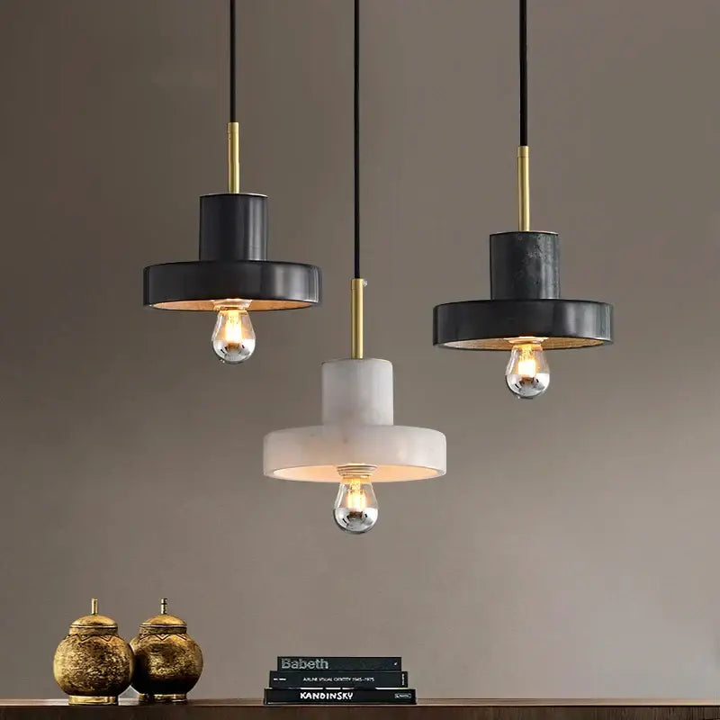 Three modern pendant lights with black and white matte shades, gold accents, and decorbites green marble details