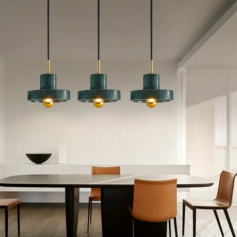 Three dark green marble pendant lights with gold accents hang above a dining table decorbites green marble design