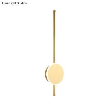 Gold-toned minimalist wall sconce with a sleek vertical rod and circular light fixture featuring warm color temperature