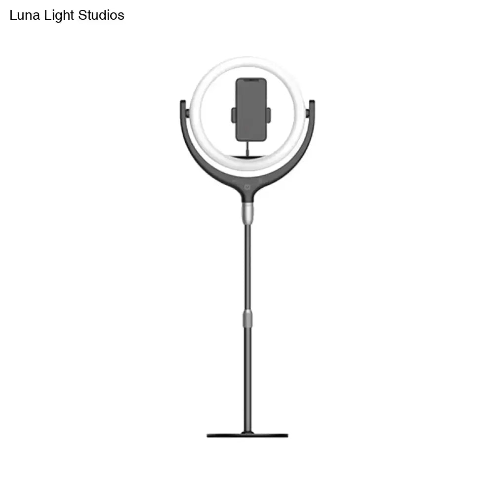 A sleek modern black and white led mirror lamp with an adjustable matte black and silver stand holding a smartphone