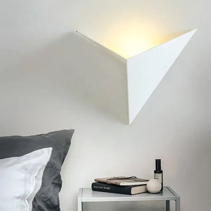 White geometric triangle sheet wall lamp emitting warm light designed as modern bedroom sconce light