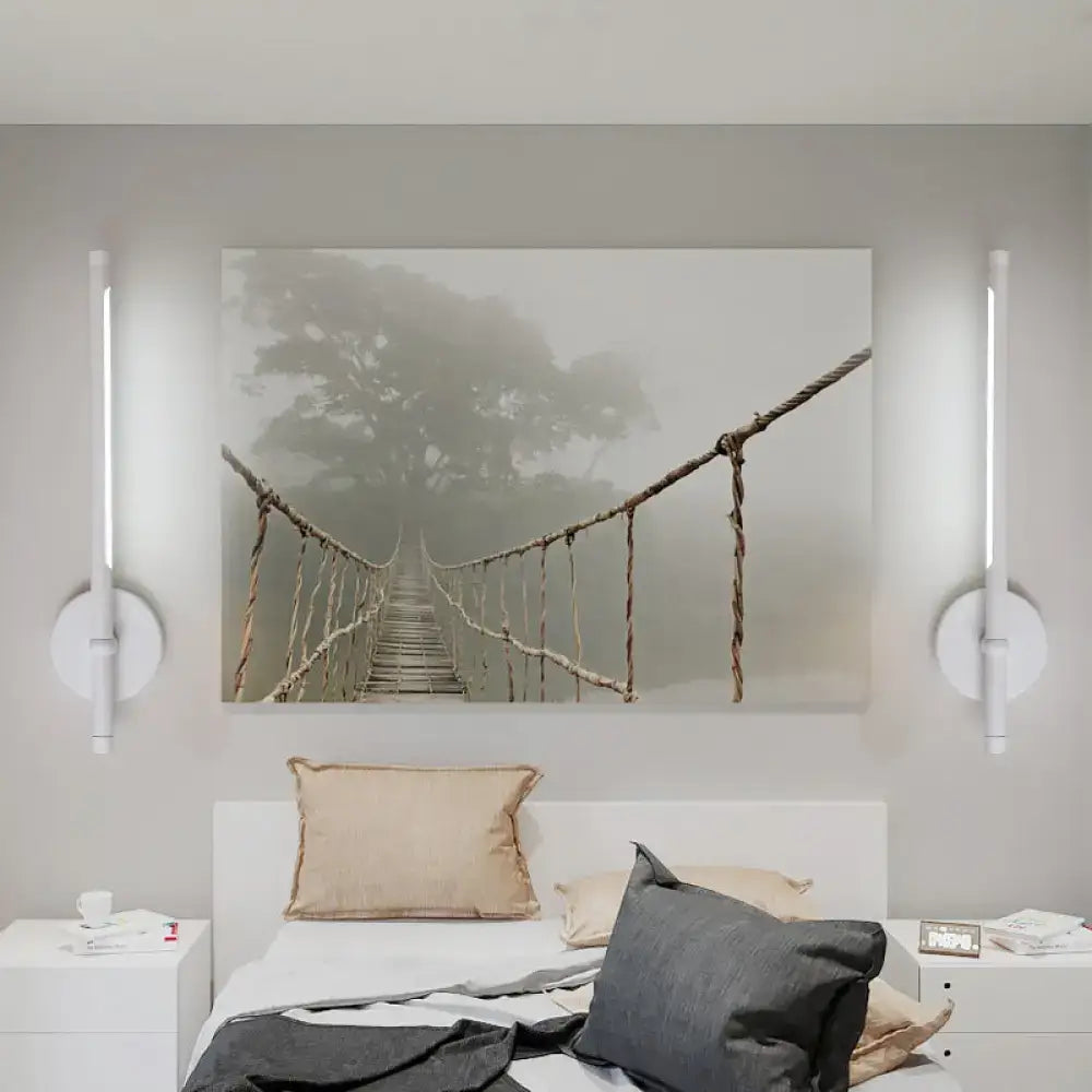 A modern black and white tubular LED sconce with direct wired installation and swing arm above bed with misty bridge print