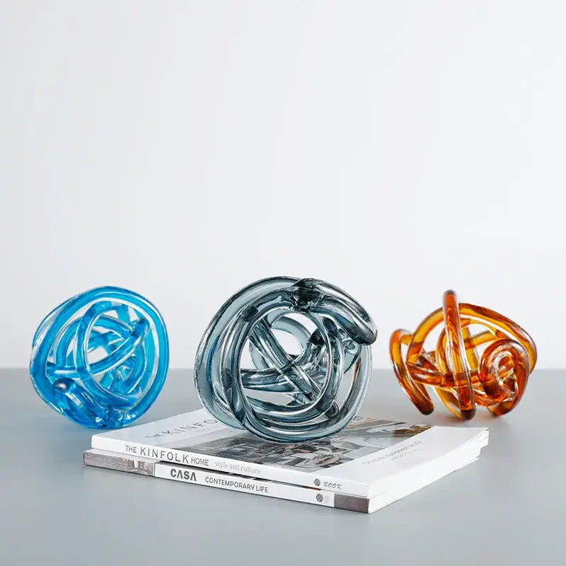 Three translucent glass coil ball decorative figurines in blue amber and gray with intricate intertwined knot designs
