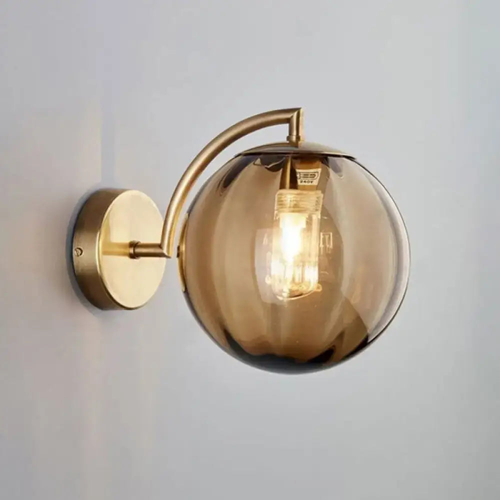 A modern wall sconce with a gold finish, brass details, and amber glass globe for bedroom lighting