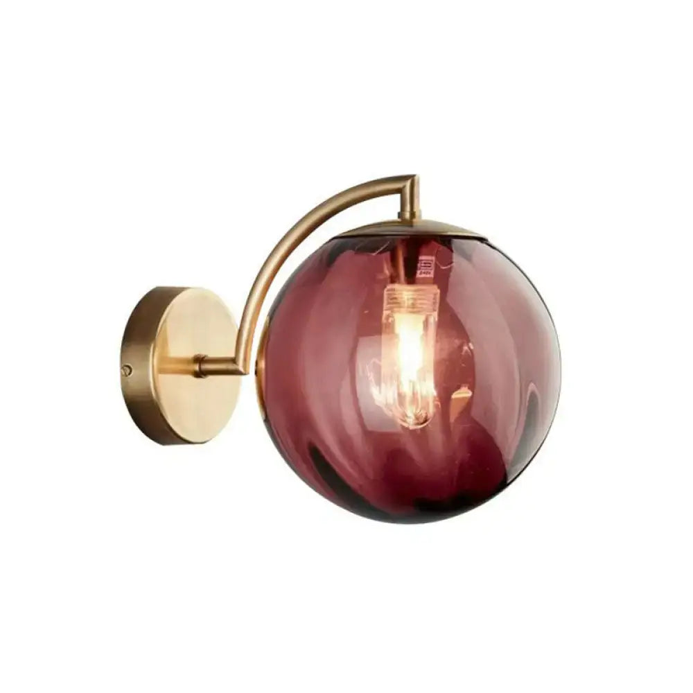 A modern amber glass wall sconce with a gold finish brushed brass bracket and curved arm for bedroom lighting